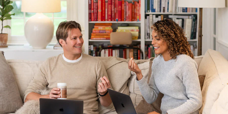 Man and woman working on laptops in a cozy living room, enjoying Charlotte's Web™ Focus Support gummies. 